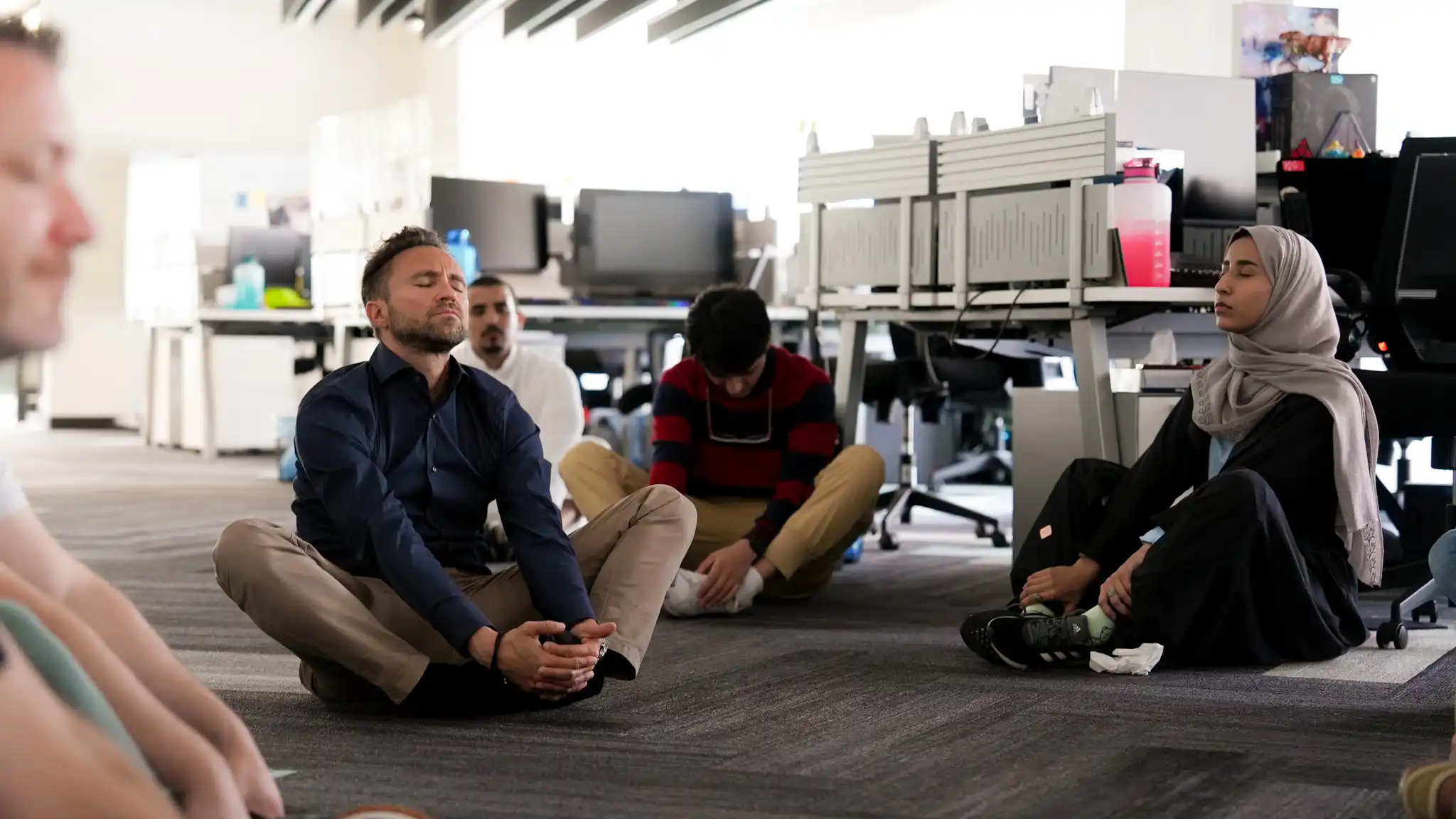 staff members sitting cross legged on the floor with their eyes closed and relaxed postures