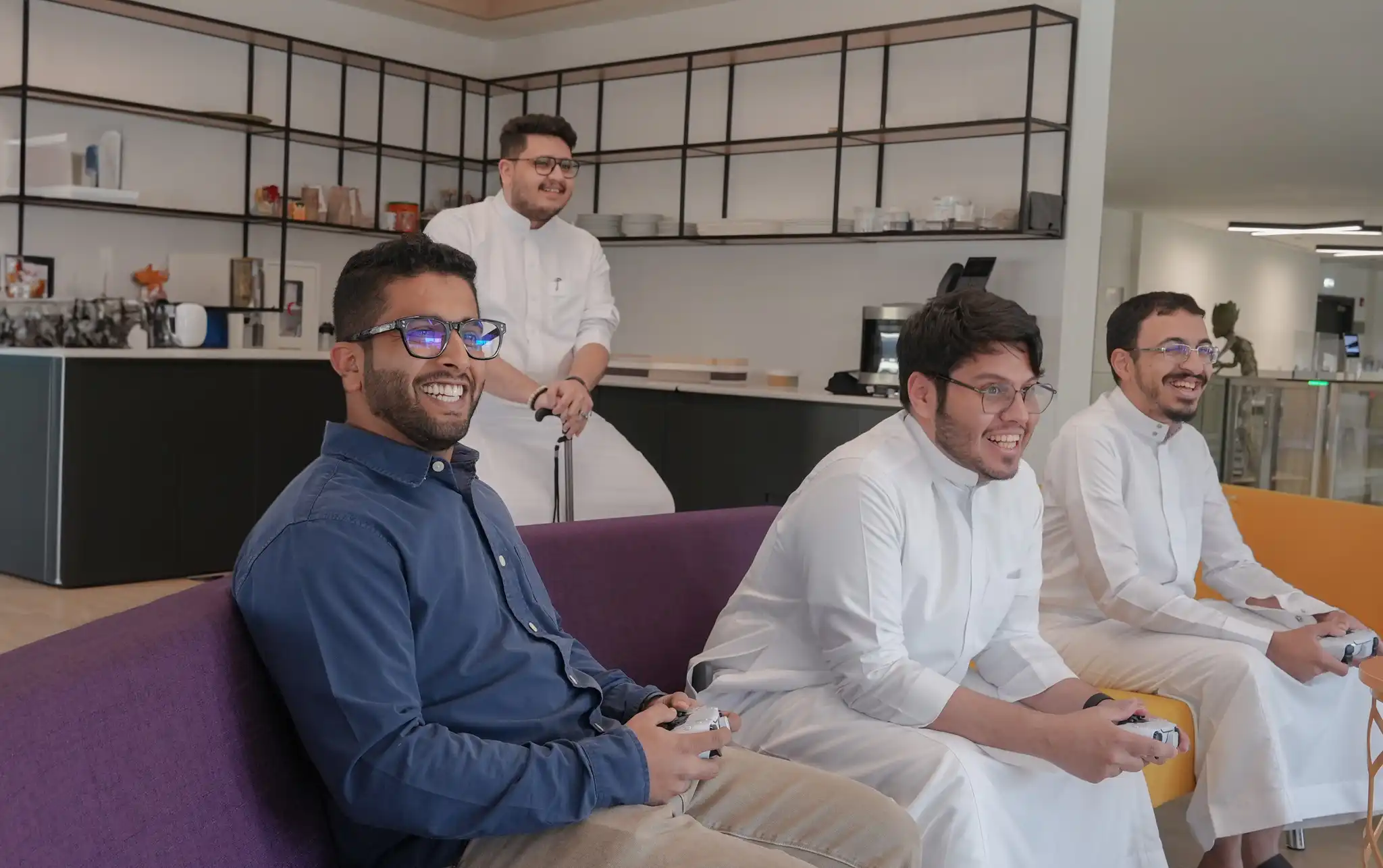 four staff members of steer studios smiling whilst playing a video game